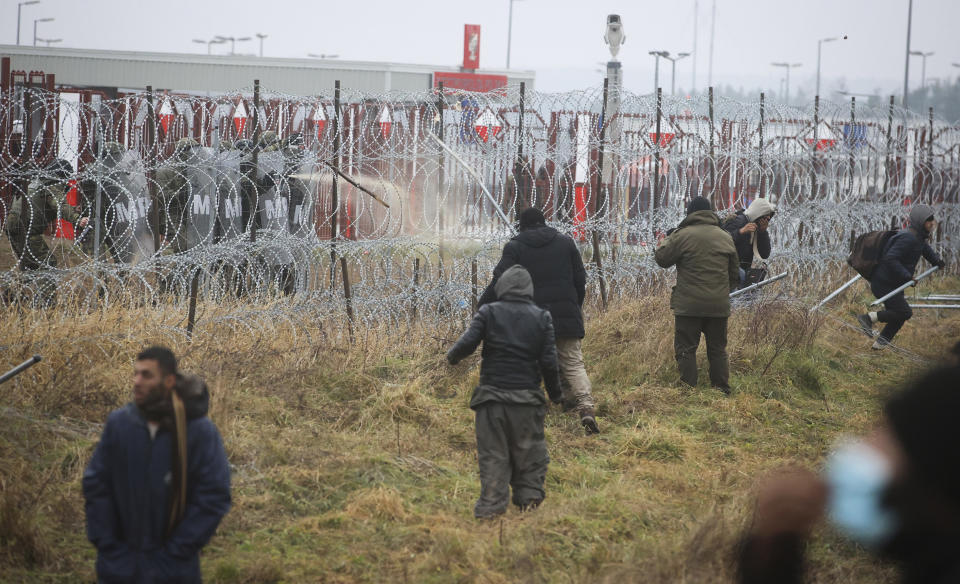Polish servicemen, top left, spray tear gas during clashes between migrants and Polish border guards at the Belarus-Poland border near Grodno, Belarus, on Tuesday, Nov. 16, 2021. Polish border forces say they were attacked with stones by migrants at the border with Belarus and responded with a water cannon. The Border Guard agency posted video on Twitter showing the water cannon being directed across the border at a group of migrants in a makeshift camp. (Leonid Shcheglov/BelTA via AP)