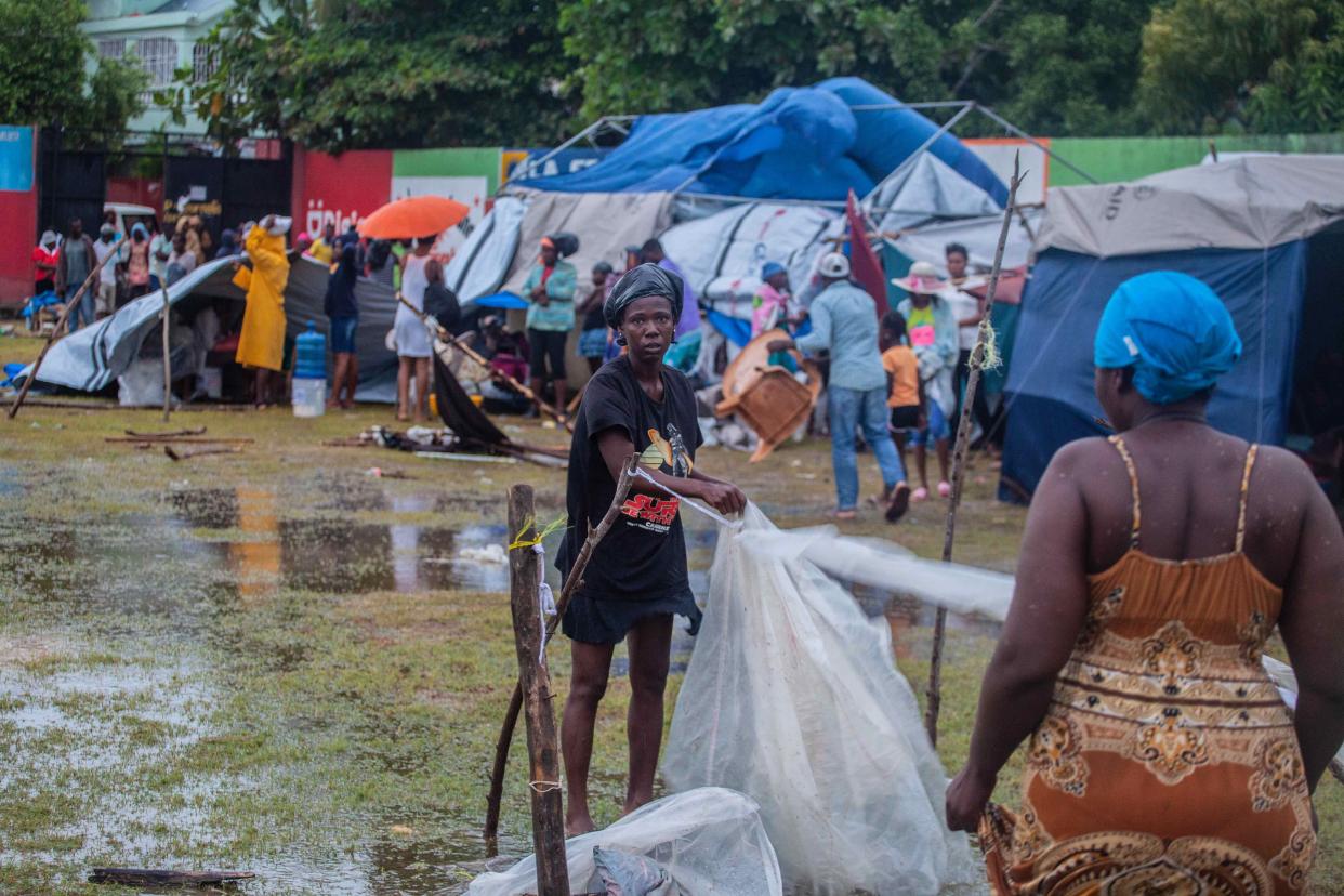 A woman works on a shelter after being hit by Tropical Storm Grace at an improvised refugee camp at Parc Lande de Gabion stadium after a 7.2-magnitude earthquake struck Haiti on Aug. 17, 2021, in Les Cayes, Haiti.