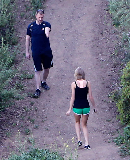 Taylor Swift goes for a hike — walking backward — in a black tank top and tiny green shorts. (Photo: INFphoto.com)