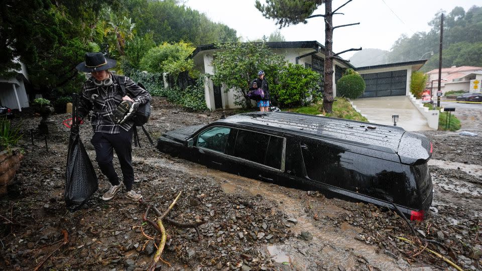 Residents evacuate past damaged vehicles after storms caused a mudslide on Monday in the Beverly Crest area of Los Angeles. - Marcio Jose Sanchez/AP