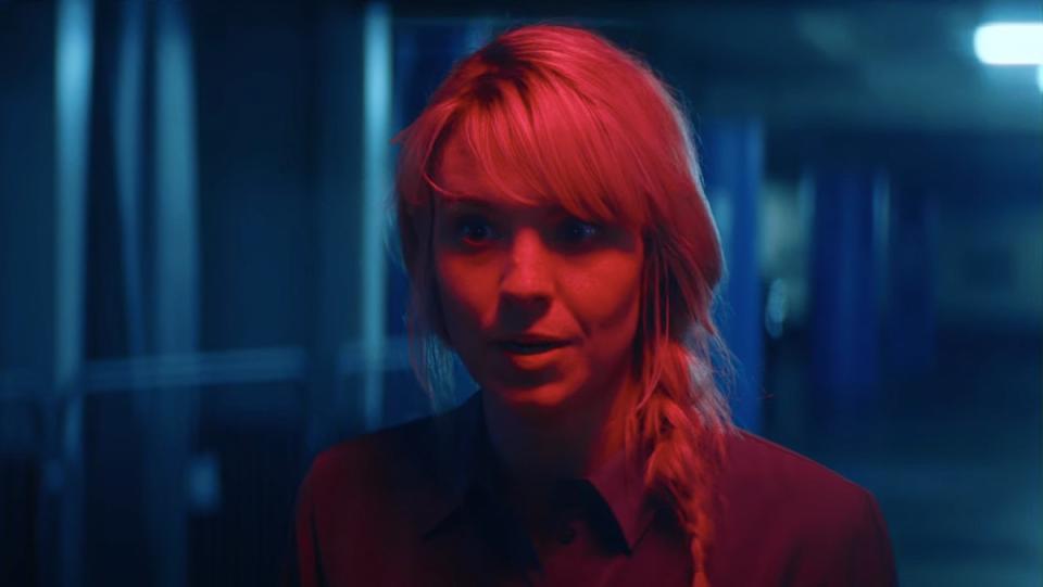 Brea Grant is drenched in red light in a scene from the film Lucky.