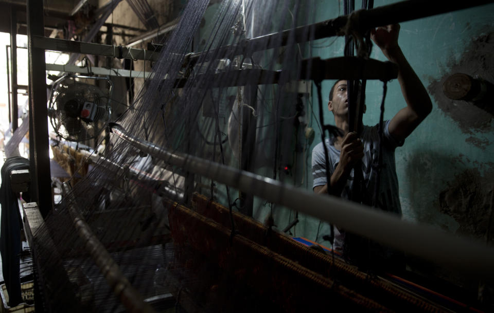 In this Saturday, July 6, 2019 photo, Palestinian worker weaves carpets on a traditional wooden loom at a carpets factory in Gaza City.Talk about old Gaza, and what pops up are images of clay pottery, colorful glassware, bamboo furniture and ancient frame looms weaving bright rugs and mats. As such professions could be dying worldwide, the pace of their declining is too fast in Gaza that out of its some 500 looms, only one is still functioning. (AP Photo/Khalil Hamra)