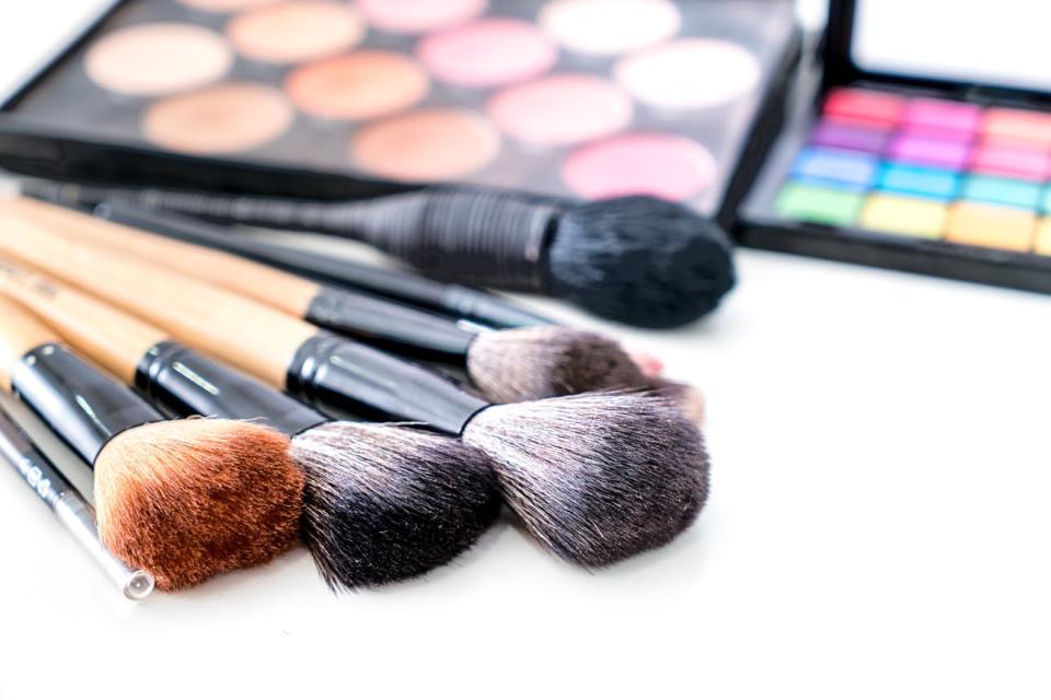 An array of makeup brushes are laid in front of a pair of palettes