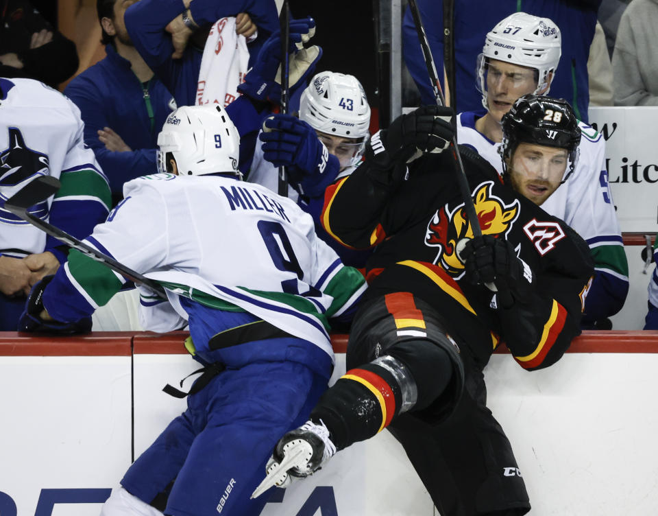 Vancouver Canucks forward J.T. Miller, left, checks Calgary Flames forward Elias Lindholm during the first period of an NHL hockey game, Saturday, Dec. 2, 2023 in Calgary, Alberta. (Jeff McIntosh/The Canadian Press via AP)