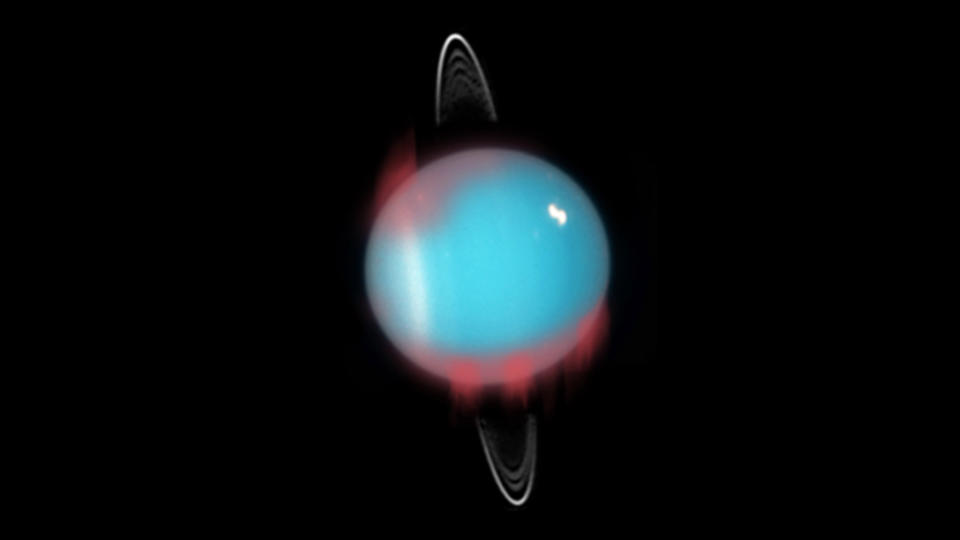 View of a blue planet with weak rings.  Red, hazy lines can be seen showing where the auroras are located.