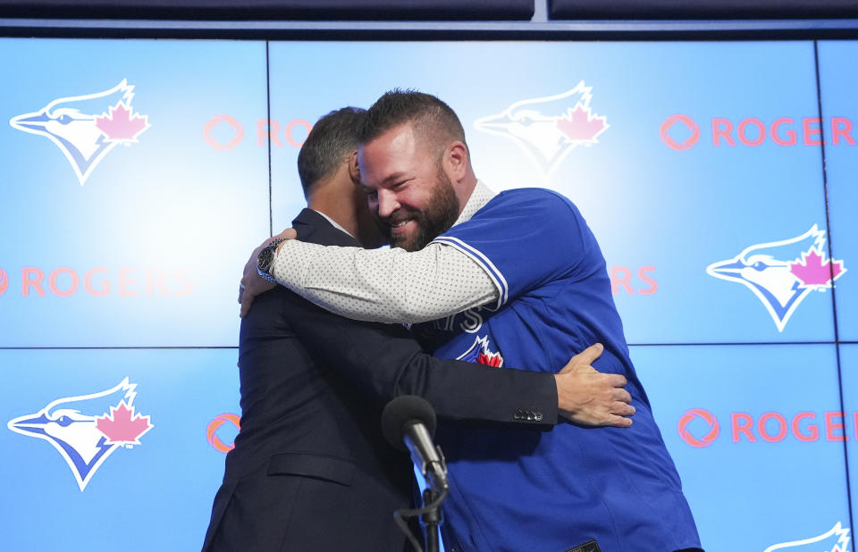 Toronto Blue Jays manager John Schneider, right, hugs general manger Ross Atkins during a press conference in Toronto on Friday, Oct. 21, 2022. The Blue Jays and manager John Schneider have agreed to terms on a three-year contract with a team option for the 2026 season, the club announced Friday. (Nathan Denette/The Canadian Press via AP)