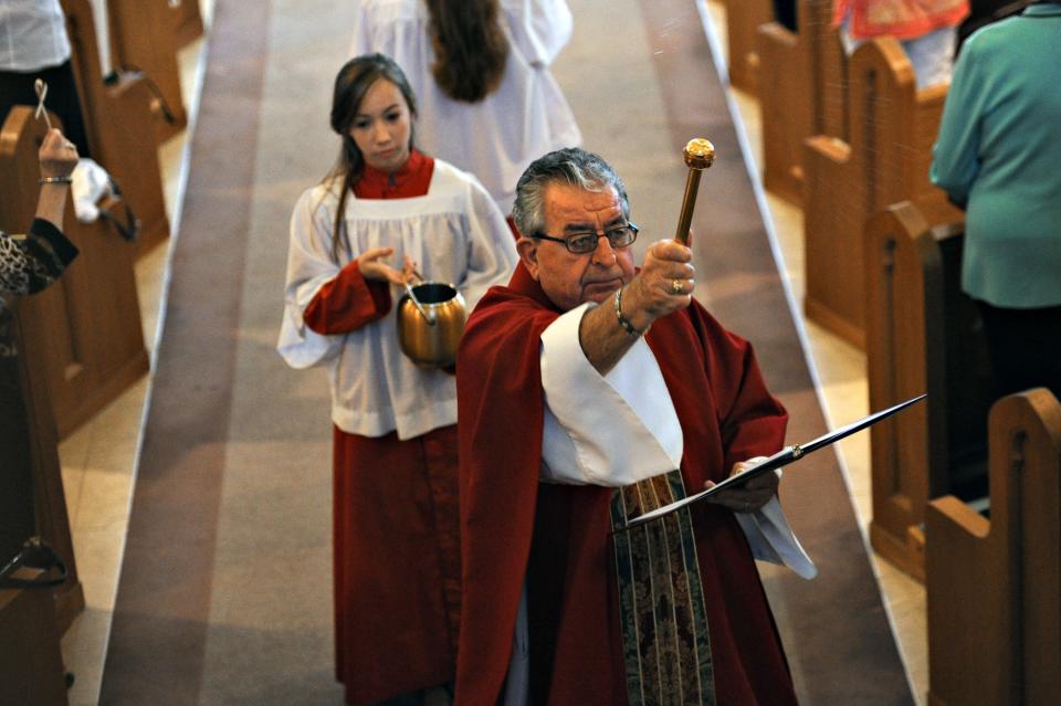 The Rev. Richard Murphy (center) blesses the palm crosses that were passed out to members of the congregation before Mass during the Solemn Entrance of Palm Sunday April 1, 2012, at Holy Cross Catholic Church in Vero Beach. Alter girl Gabrielle Diskin holds the holy water.