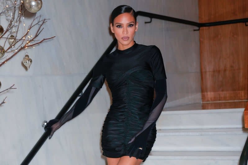 Cassie wearing a fitted black dress with mesh sleeves and black ankle boots, posing on a staircase