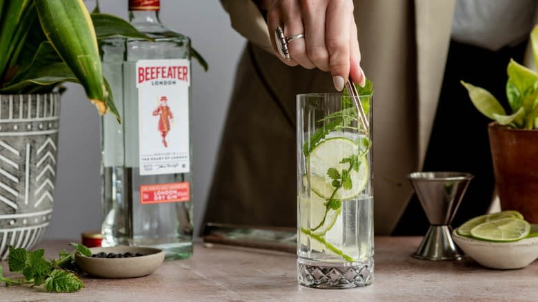 A hand stirring lime balm into a cocktail 