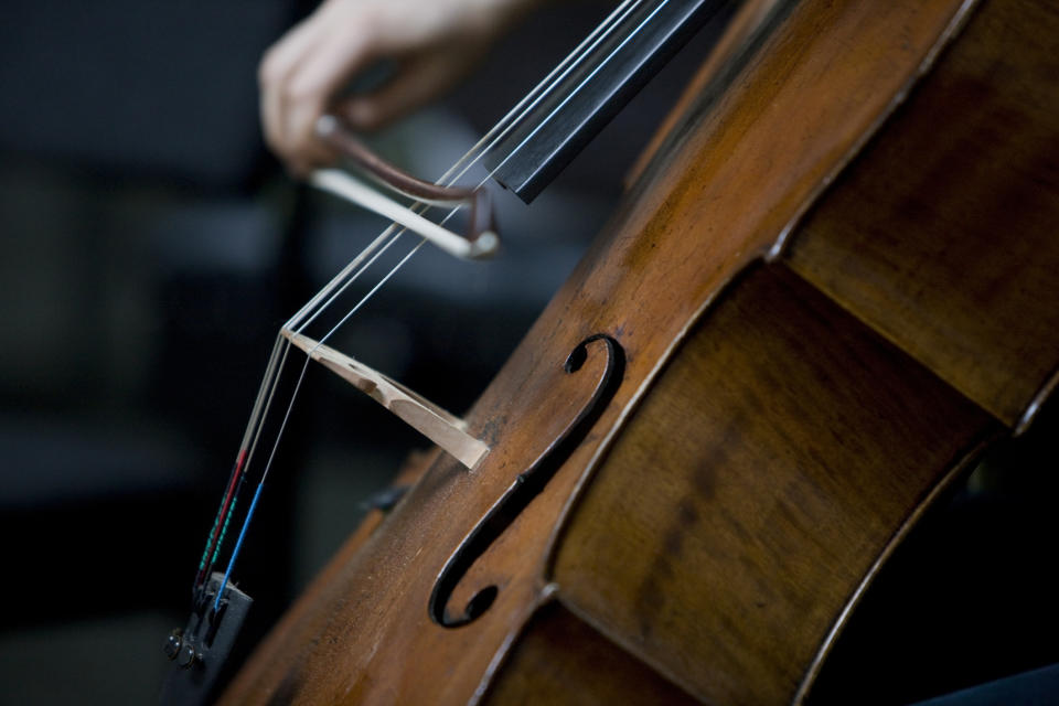 Close-up of a person's hand playing the cello with a bow, focusing on strings and f-holes