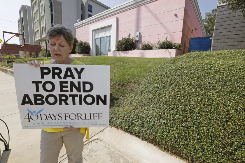 FILE - In this Oct. 2, 2019 file photo, an abortion opponent sings to herself outside the Jackson Womens Health Organization clinic in Jackson, Miss. Three judges from a conservative federal appeals court are hearing arguments, Monday, Oct. 7, over a Mississippi law that would ban most abortions after 15 weeks of pregnancy. Republican Gov. Phil Bryant signed the law in 2018, the state's only abortion clinic immediately sued and U.S. District Judge Carlton Reeves blocked the law from taking effect. (AP Photo/Rogelio V. Solis)