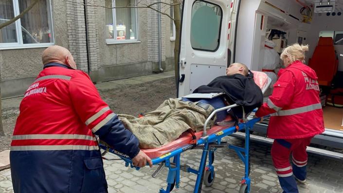 A stretcher carrying a wounded person is loaded into an ambulance by two emergency workers.