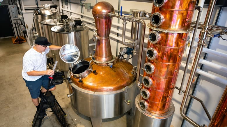 A man working at a craft distillery next to two stills