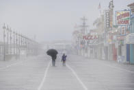 A man shields himself from the rain with an umbrella as he walks along with a child during a rainy and foggy winter afternoon at the Ocean City boardwalk in Ocean City, N.J. (Jose F. Moreno/The Philadelphia Inquirer via AP)