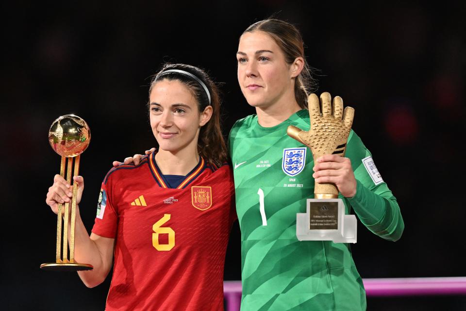 Spain's midfielder #06 Aitana Bonmati (L) holding the trophy on the podium for the FIFA Golden Ball Award embraces England's goalkeeper #01 Mary Earps holding the FIFA Golden Glove Award after the Australia and New Zealand 2023 Women's World Cup final football match between Spain and England at Stadium Australia in Sydney on August 20, 2023. (Photo by Izhar KHAN / AFP) (Photo by IZHAR KHAN/AFP via Getty Images)