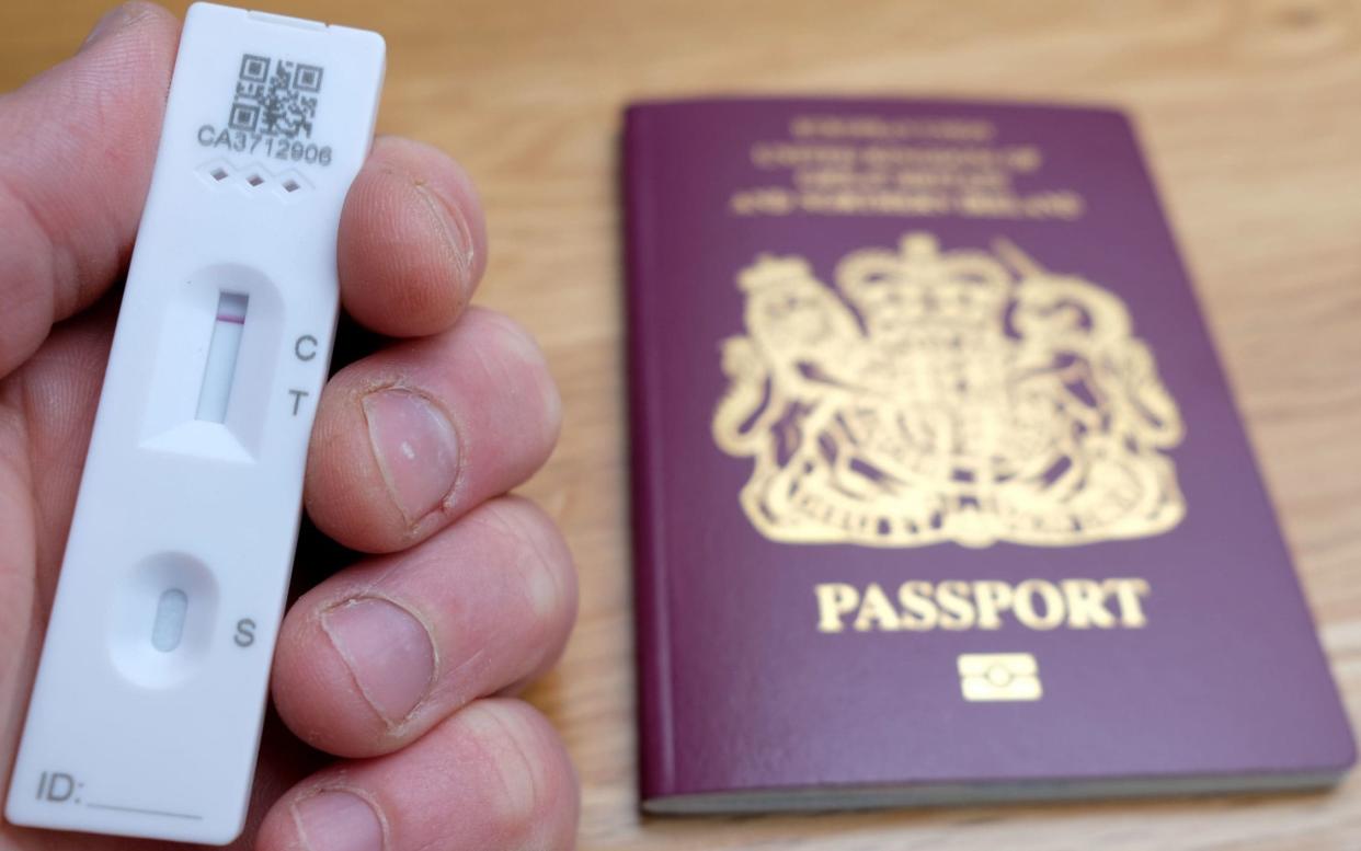 A person holding a negative lateral flow Covid test in front of a passport - PA