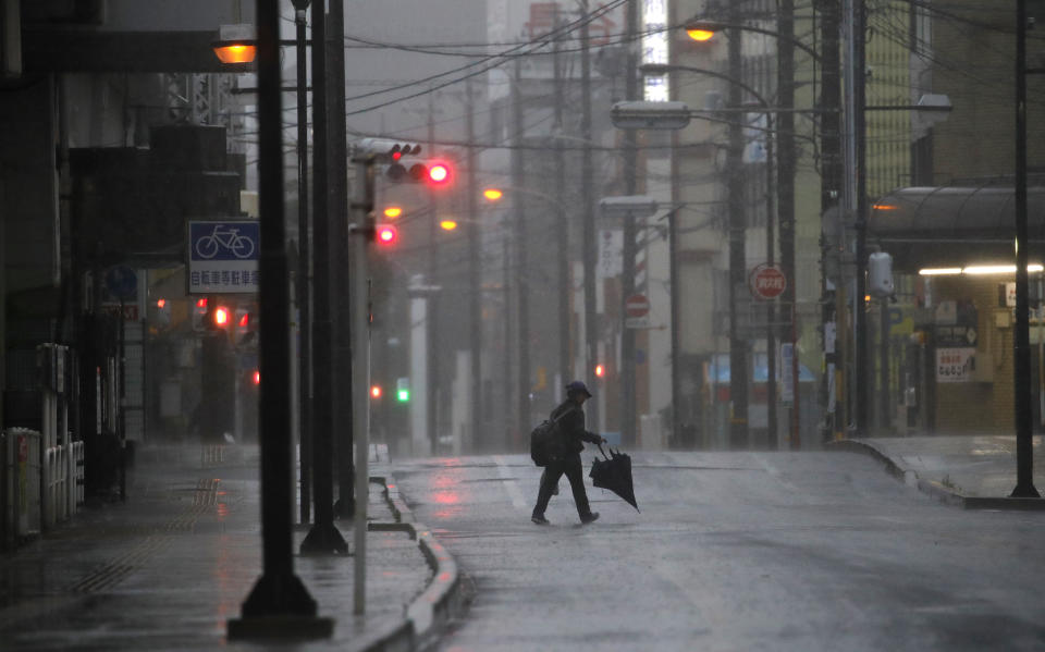 A woman crosses the road in Hamamatsu, central Japan, Saturday, Oct. 12, 2019. A heavy downpour and strong winds pounded Tokyo and surrounding areas on Saturday as a powerful typhoon forecast as the worst in six decades approached landfall, with streets and train stations deserted and shops shuttered. (AP Photo/Christophe Ena)