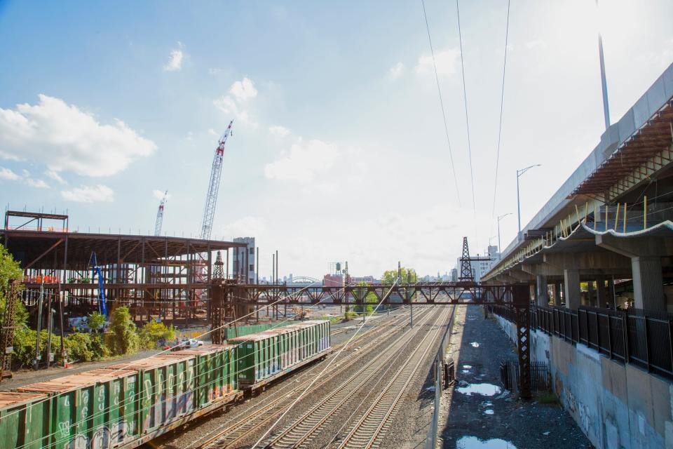 A large warehouse being constructed next to train tracks with the New York City skyline in the distance.