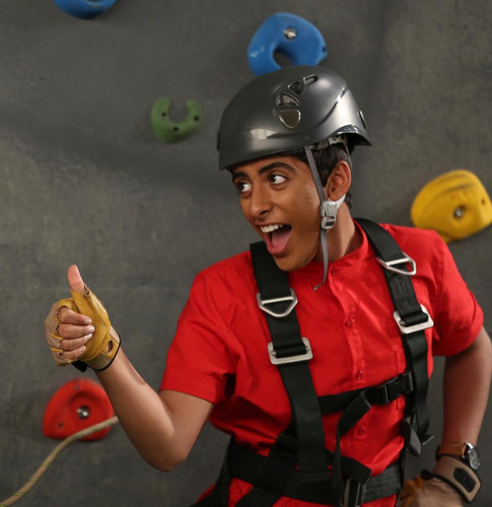 Ravi in helmet and harness giving a thumbs-up in front of a climbing wall