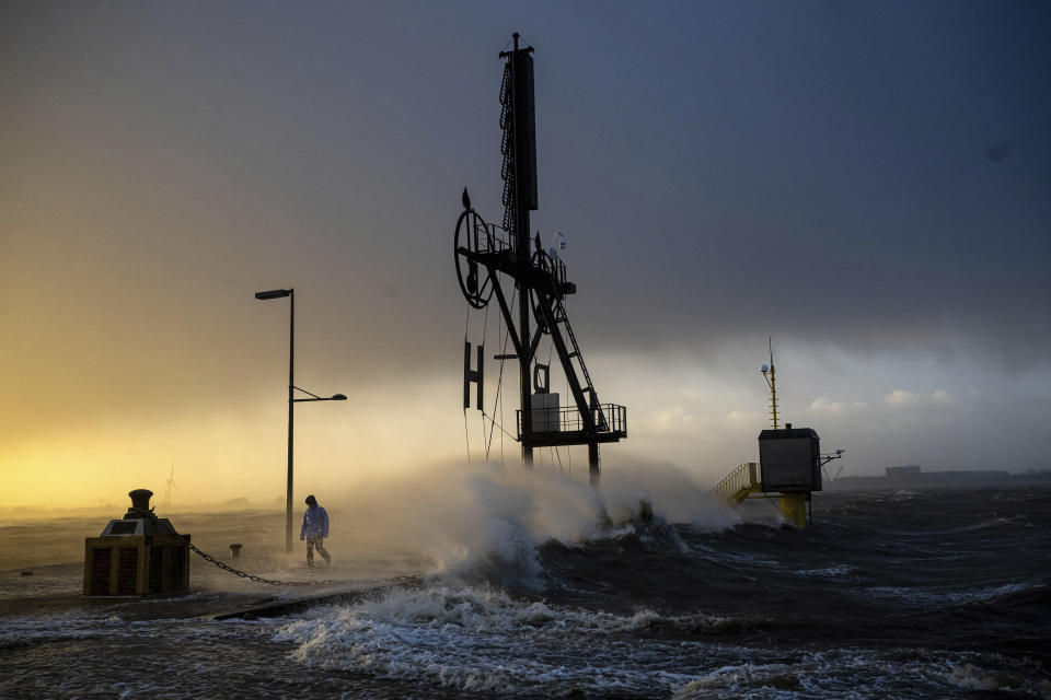 A person walks along the banks of the Weser estuary during a storm surge and waves in Bremerhaven, Germany, Friday Dec. 22, 2023. Pre-Christmas rail travelers in parts of Germany faced widespread disruption on Friday as a storm swept across northern Europe, bringing down trees and prompting warnings of flooding on the North Sea coast. (Sina Schuldt/dpa via AP)