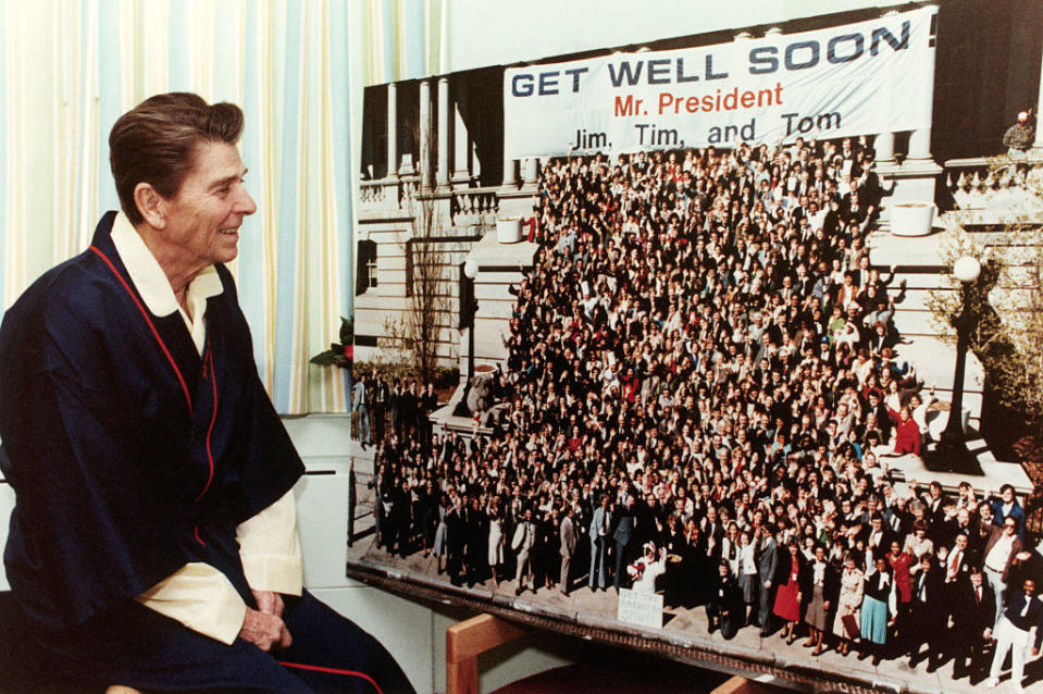 Reagan looking at people and a sign that says, "Get well soon, Mr President"