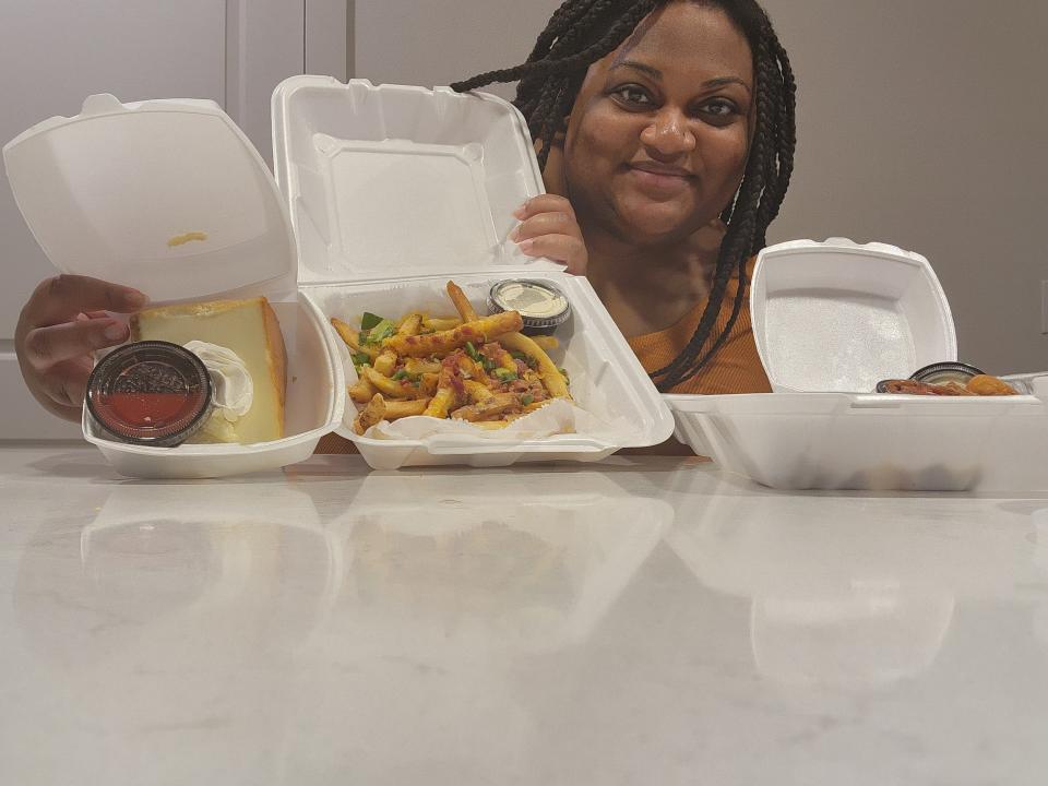 The writer poses with takeout containers of fries and cheesecake from Logan's Roadhouse