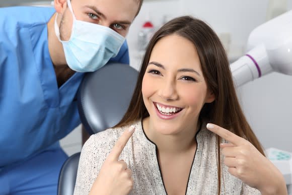 Dentist posing with smiling patient pointing to white teeth