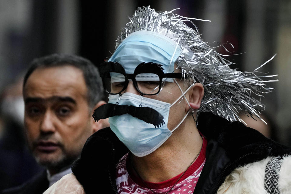 A man wearing face masks with a mustache attached, walks down Regents Street in London, Thursday, Dec. 23, 2021. British Prime Minister Boris Johnson said on Monday that his government reserves the "possibility of taking further action" to protect public health as Omicron spreads across the country. (AP Photo/Frank Augstein)