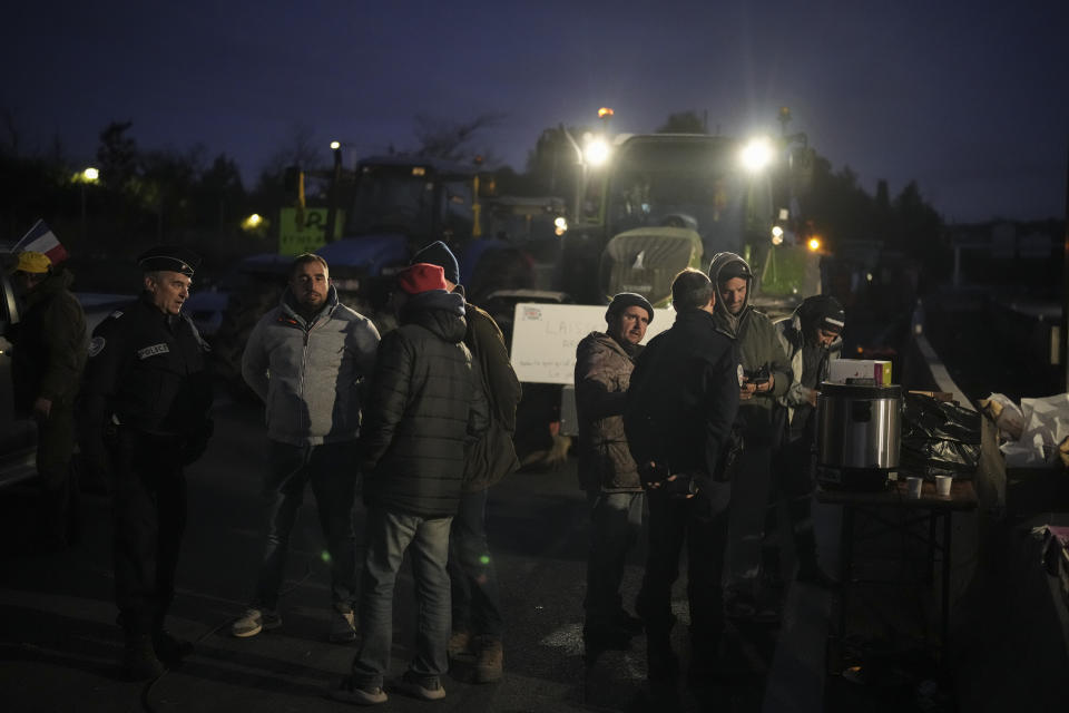 Farmers have breakfast after spending the night at a highway barricade in Aix-en-Provence, southern France, Tuesday, Jan. 30, 2024. France's protesting farmers encircled Paris with traffic-snarling barricades Monday, using hundreds of lumbering tractors and mounds of hay bales to block highways leading to France's capital to pressure the government over the future of their industry. (AP Photo/Daniel Cole)