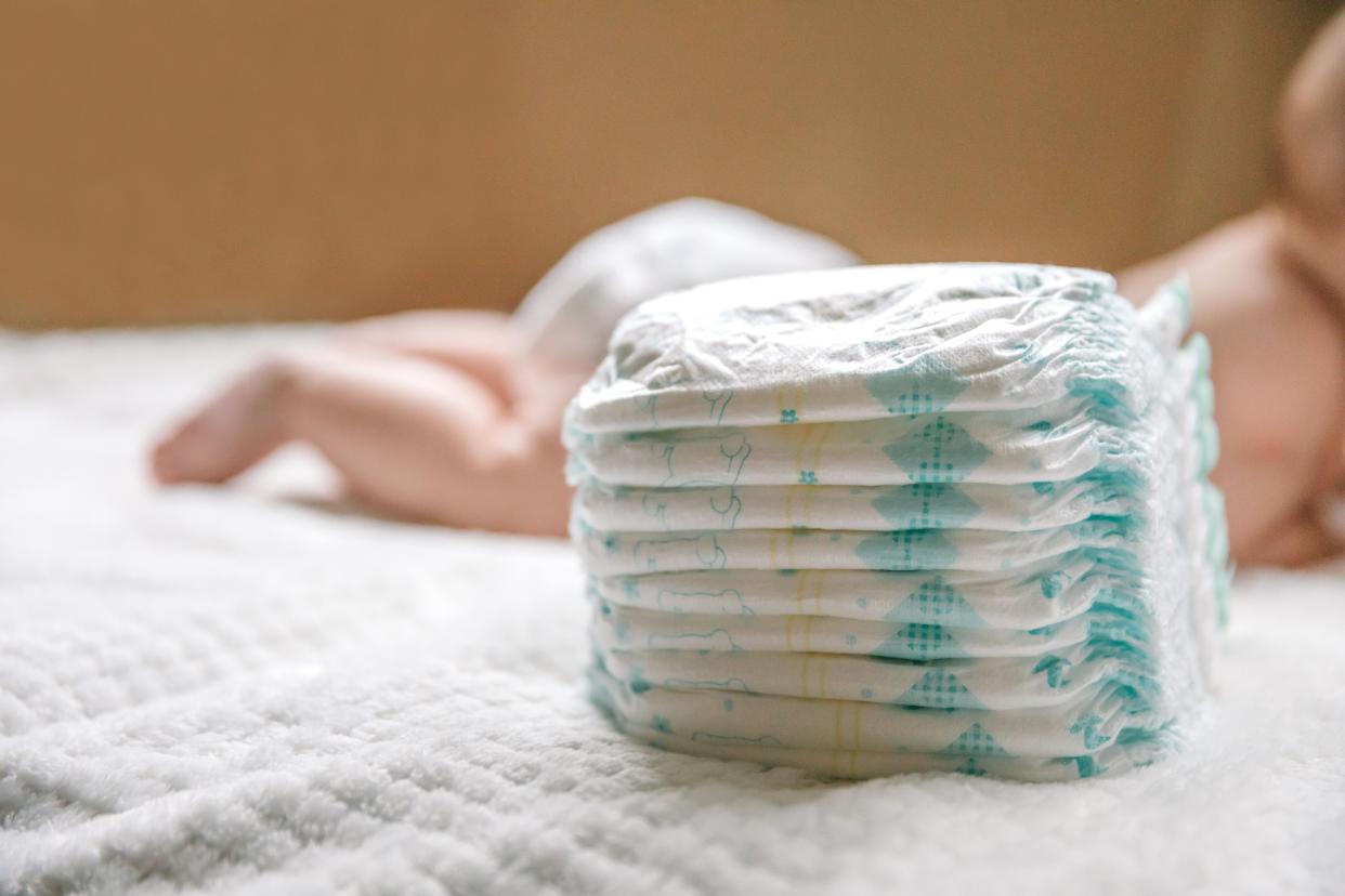 Stack of disposable diapers with baby in the background.