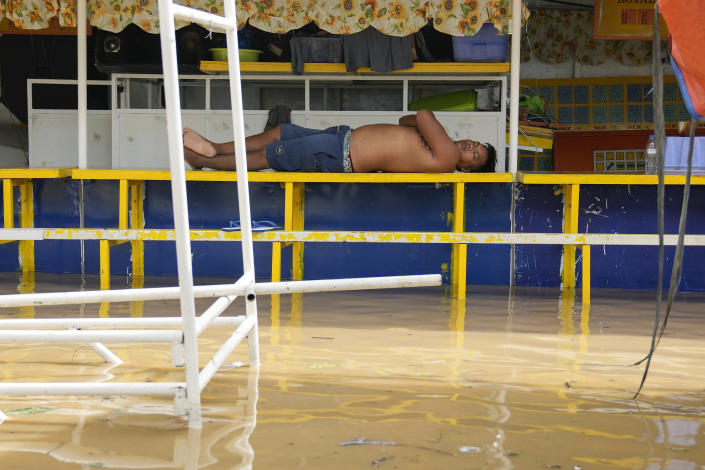 A man sleeps at his flooded stall from to Typhoon Noru in San Miguel town, Bulacan province, Philippines, Monday, Sept. 26, 2022. Typhoon Noru blew out of the northern Philippines on Monday, leaving some people dead, causing floods and power outages and forcing officials to suspend classes and government work in the capital and outlying provinces. (AP Photo/Aaron Favila)