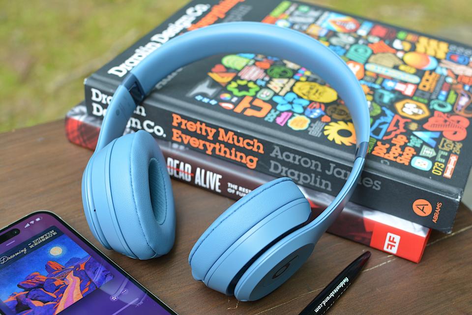 Beats Solo 4 apoiado em dois livros com um iPhone à esquerda e uma caneta preta em primeiro plano. 