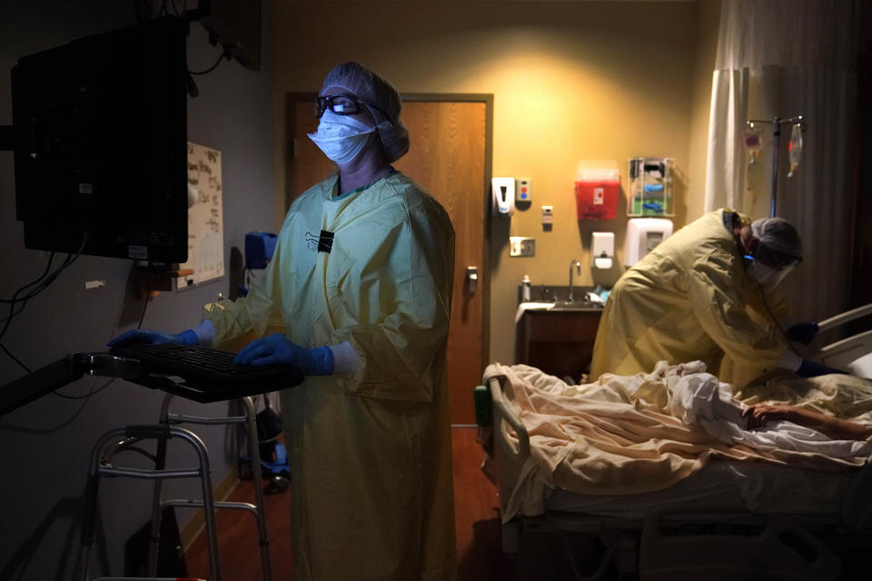 Registered nurse Shelly Girardin, left, is illuminated by the glow of a computer monitor as Dr. Shane Wilson examines COVID-19 patient Neva Azinger inside Scotland County Hospital on Tuesday, Nov. 24, 2020, in Memphis, Mo. The coronavirus pandemic largely hit urban areas first, but the autumn surge is now ravaging rural America, stressing the staffs of tiny hospitals like the one in Scotland County. (AP Photo/Jeff Roberson)