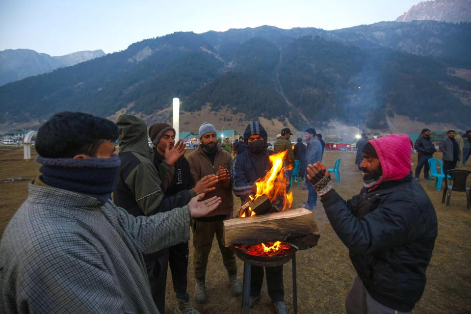 People warm themselves near a small fire as they attend the celebrations in Sonamarg, Indian Kashmir (EPA)