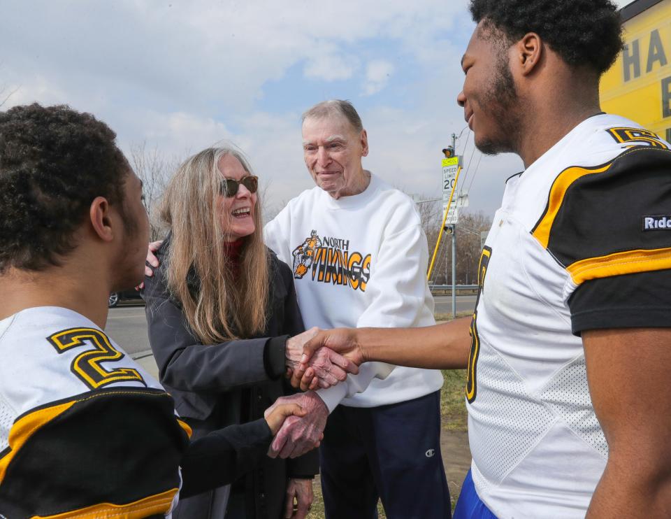 North High School football players Elijah Gervins, left, and Tyreon Jones greet 1944 graduate John Collver and his daughter Cynthia Martinez in front of a message board wishing Collver a happy 97th birthday on Friday in Akron.