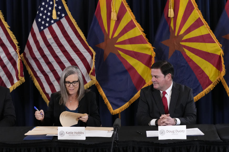 Katie Hobbs, the Democratic governor-elect and current secretary of state, left, signs the official certification for the Arizona general election canvass as Arizona Republican Gov. Doug Ducey, right, looks on during a ceremony at the Arizona Capitol in Phoenix, Monday, Dec. 5, 2022. (AP Photo/Ross D. Franklin, Pool)