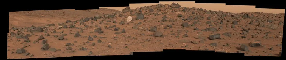 a rocky, rust colored barren, hilly landscape littered with various rocks and brown dust.