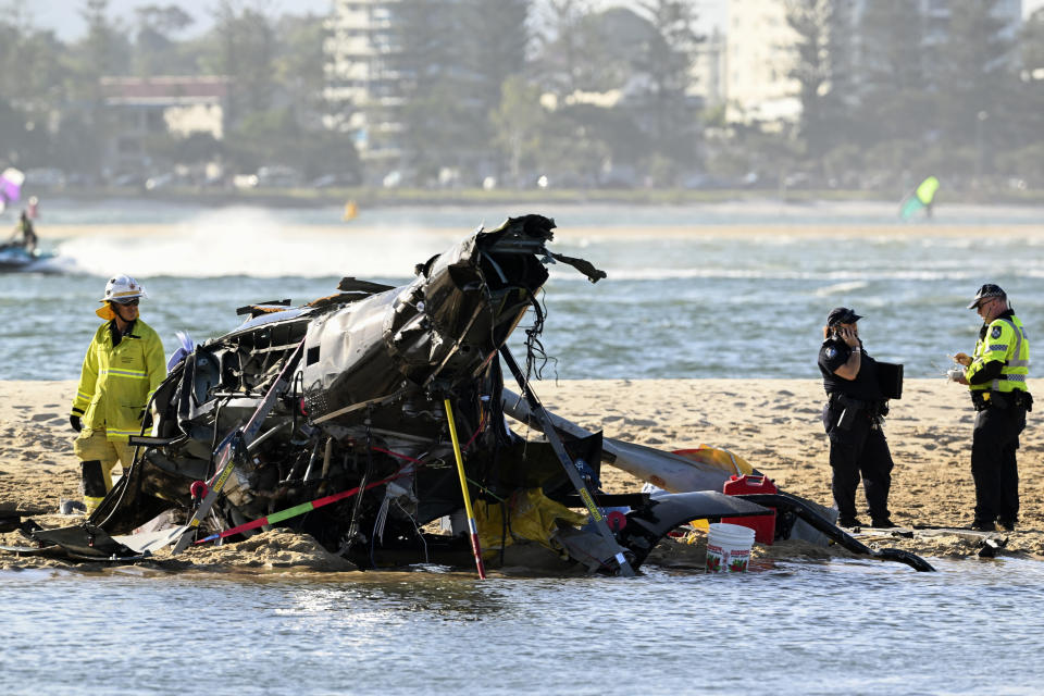 Emergency workers inspect a helicopter at a scene collision near Seaworld, on the Gold Coast, Australia, Monday, Jan. 2, 2023. Two helicopters collided killing several passengers and critically injuring a few others in a crash that drew emergency aid from beachgoers enjoying the water during the southern summer. (Dave Hunt/AAP Image via AP)