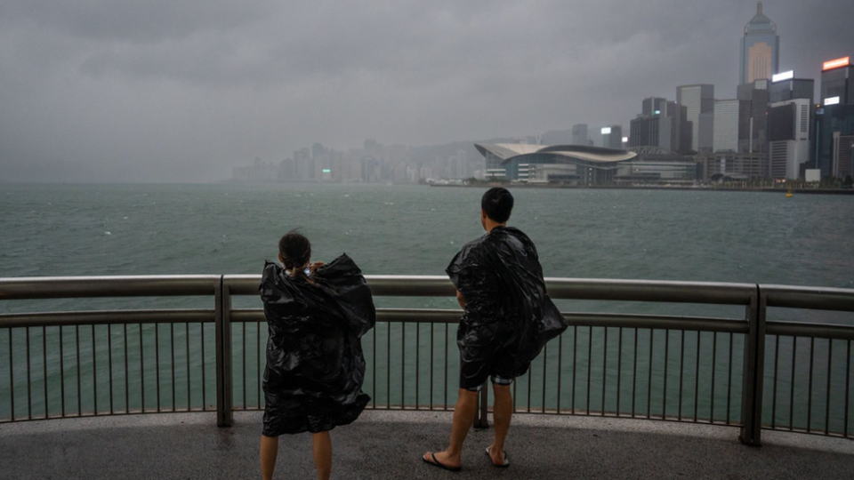 A couple wearing black garbage bags as rain jackets stand facing a storm at Hong Kong's harbour on 1/9/23