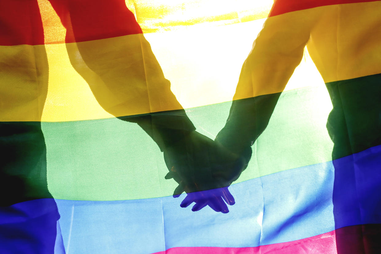 People, homosexuality, same-sex marriage, gay and love concept - close up of happy male gay couple hugging and holding rainbow flag