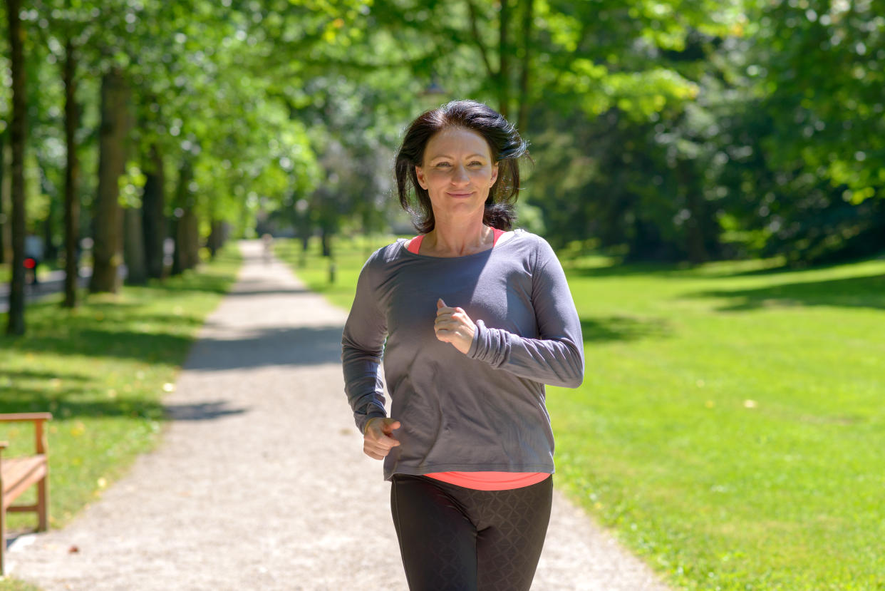 Smiling woman jogging towards the camera in a park  in a healthy active lifestyle concept