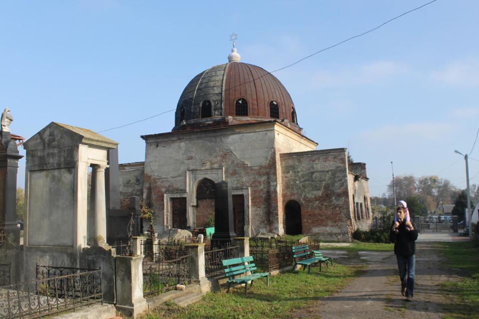 In this photo taken on Oct. 22 2012, a man carrying a child walks past an abandoned Synagogue on the Jewish cemetery in Chernivtsi, a city of 250,000 in southwestern Ukraine. Known as the Little Paris or, alternatively, the Little Vienna of Ukraine, Chernivtsi is a perfect place for a quiet romantic weekend trip and a crash course in the painful history of Europe in the 20th century. (AP Photo/Maria Danilova)