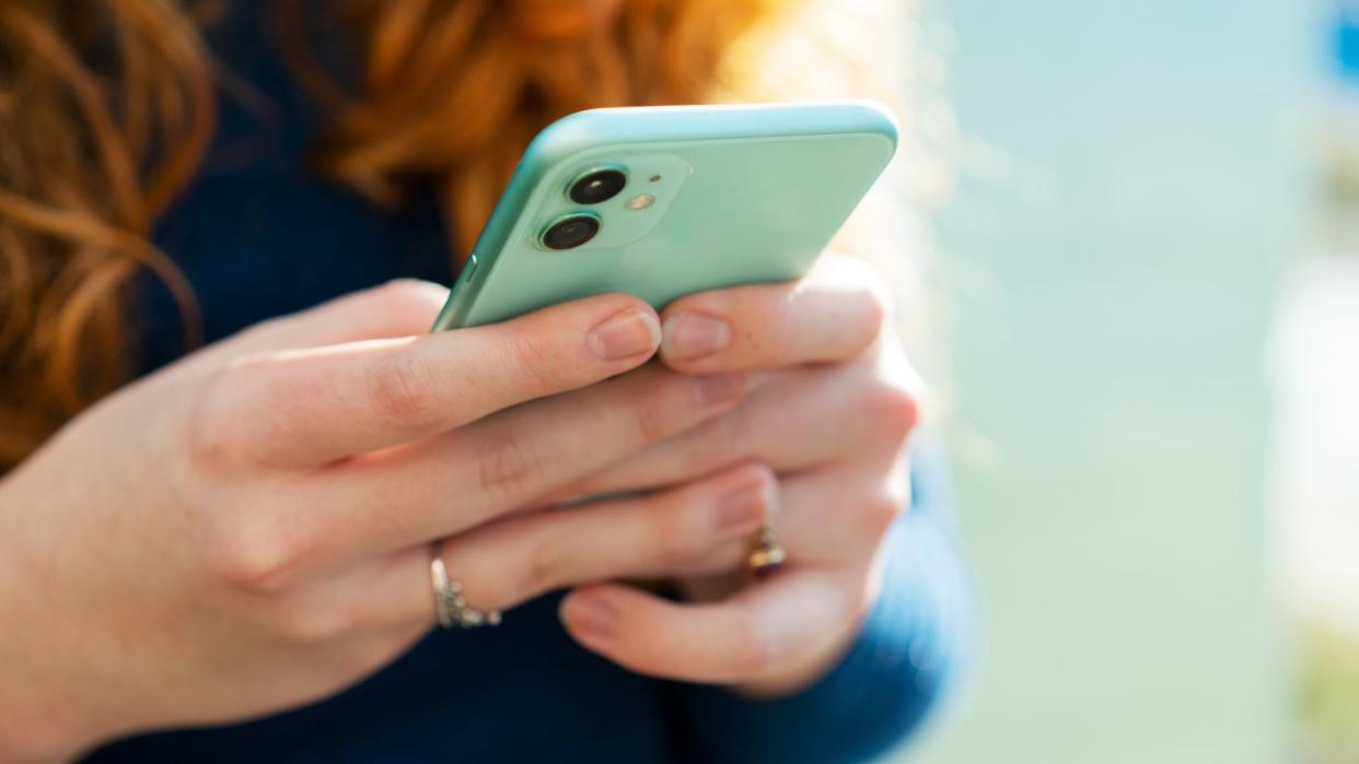  Close up on a young woman's hands as she's holding a phone with its screen away from the camera. 
