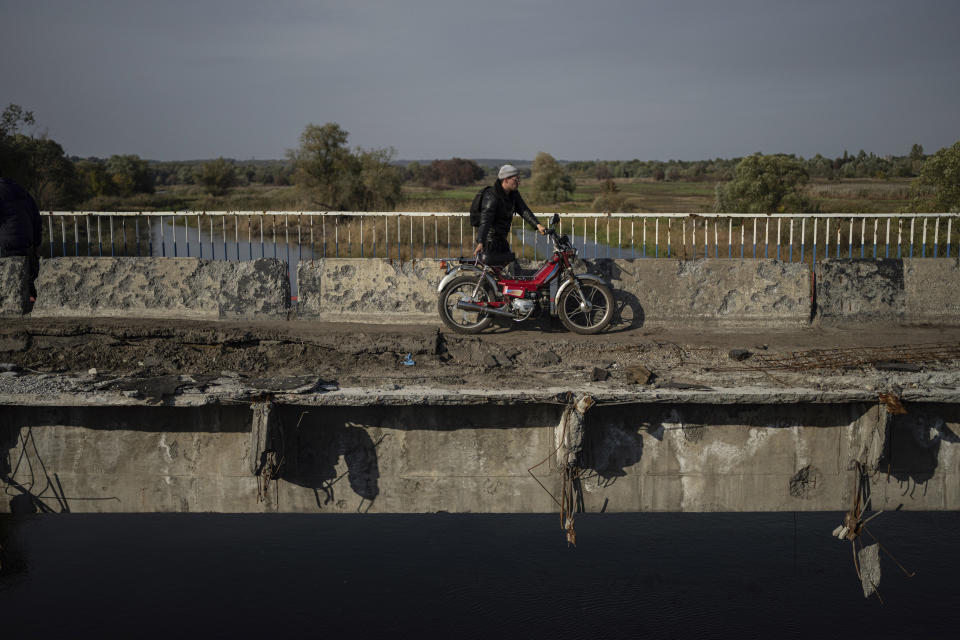 A man hauls his motorbike on a destroyed bridge across Oskil river during evacuation in recently liberated town Kupiansk, Ukraine, Saturday, Oct. 1, 2022. (AP Photo/Evgeniy Maloletka)