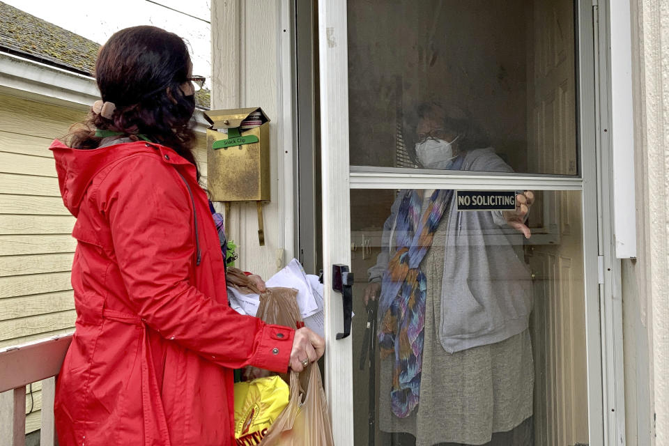 Senior citizen Barbara Bender answers the door for Store to Door employee Nancy Murphy in Portland, Ore., as she delivers an order of groceries for the nonprofit on Feb. 25, 2021. An untold number of older people are getting left behind in the desperate dash for shots because they are too frail, overwhelmed, isolated or poor to navigate a system that favors healthier individuals with more resources. Nonprofits, churches and health care outreach workers are scrambling to to reach older people who are falling through the cracks before the nation’s focus moves on and the competition for vaccines stiffens. (AP Photo/Gillian Flaccus)