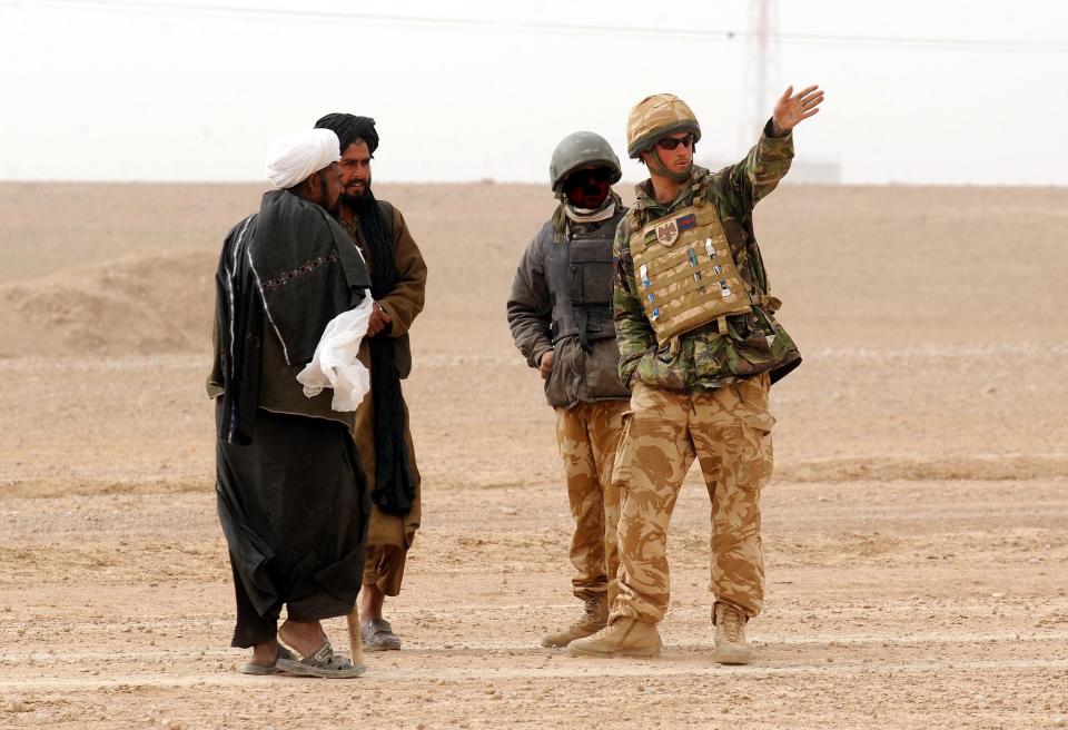 Prince Harry, seen in the Afghan desert, points his arm as three men look on.