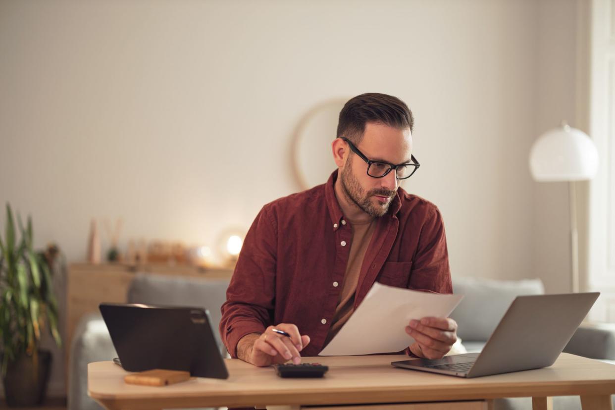 Man working on some financial problems, looking at the laptop, holding a document.