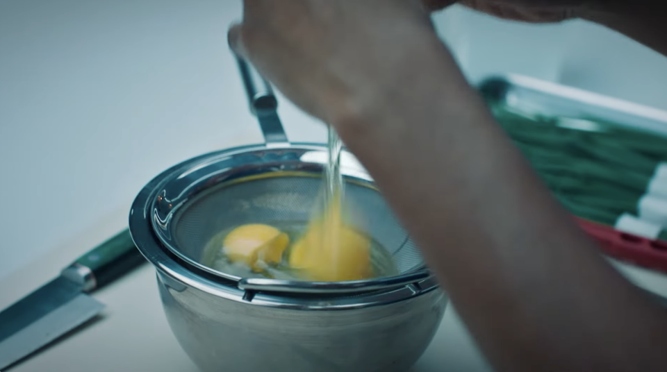 Sydney from The Bear cracking eggs into a mesh sieve