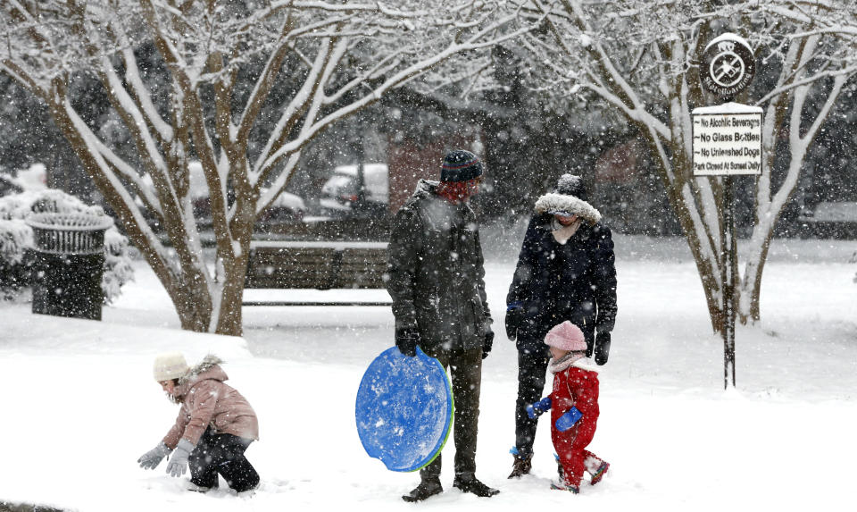 Aaron Savage and wife Bonnie Wright watch as their children Mabel Savage, 4, left, and Sadie Savage, 2, play in the snow during a winter storm on Sunday, Jan. 31, 2021, in Richmond, Va. (Joe Mahoney/Richmond Times-Dispatch via AP)