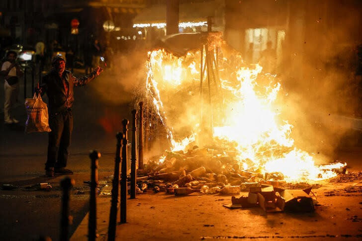 Un hombre gesticula junto a un contenedor en llamas mientras la gente protesta tras la muerte de Nahel, un adolescente de 17 años, que falleció tras disaparos de un policía francés en Nanterre, en París, Francia